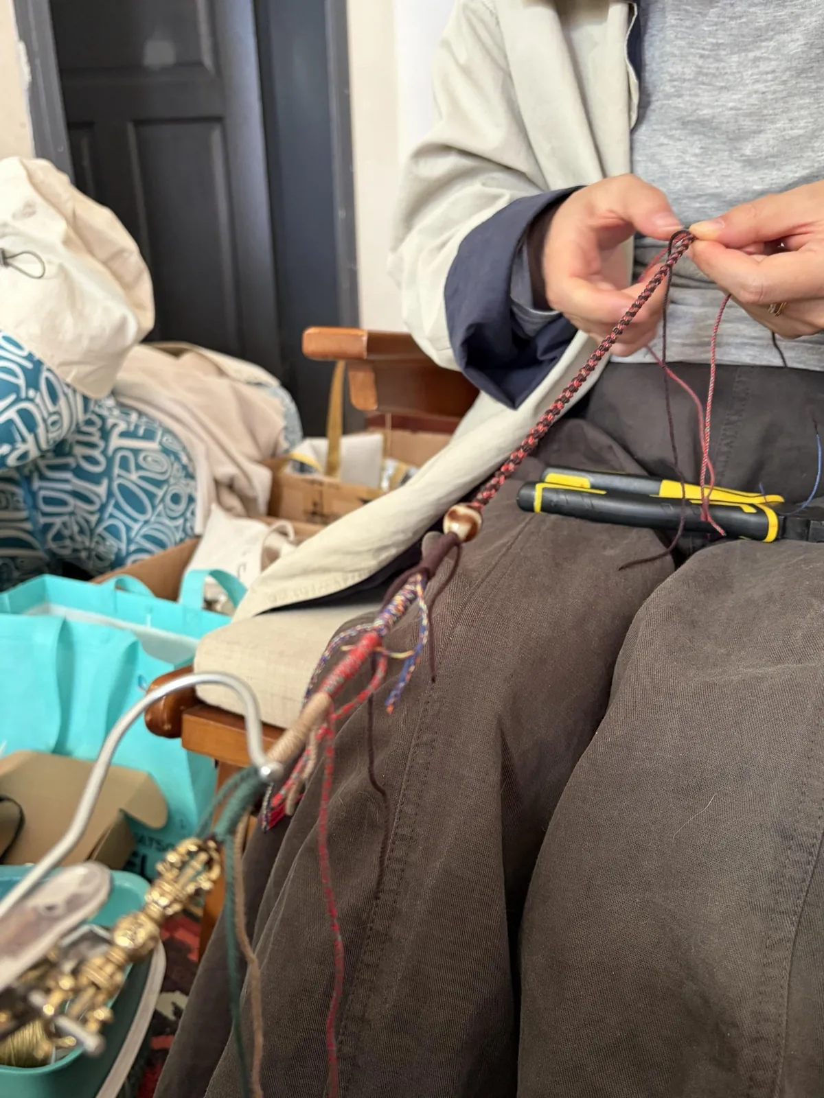Hands working with cord and jewelry tools at a workbench