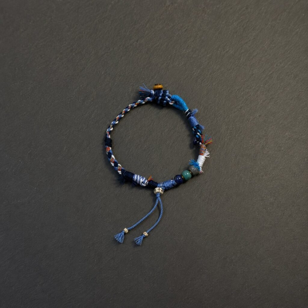 LHARI Blue Wind Prayer Cord Bracelet black background overhead view