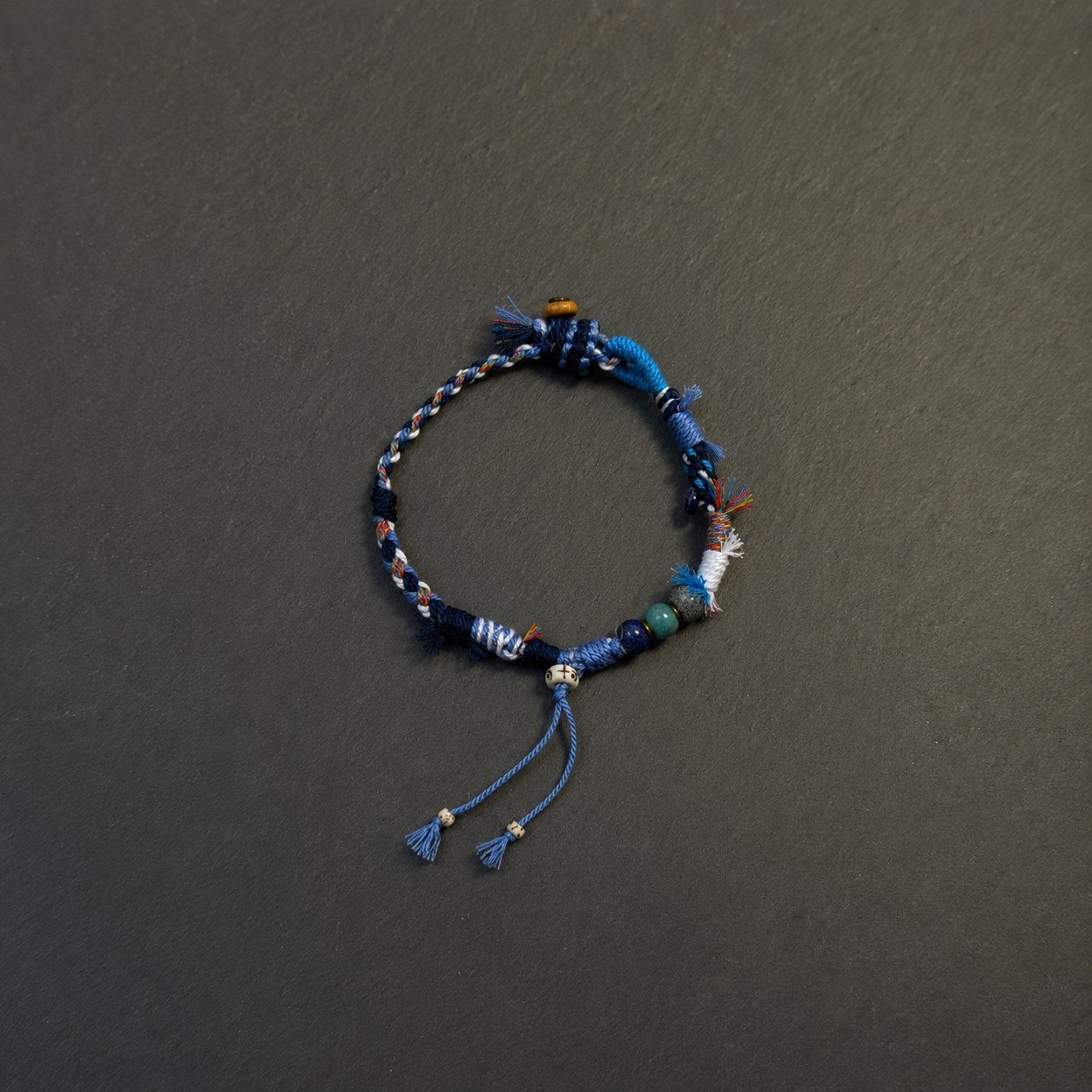 LHARI Blue Wind Prayer Cord Bracelet black background overhead view